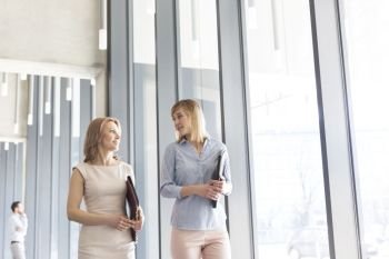 Businesswomen with files talking while walking in corridor by office