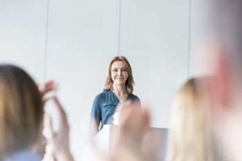 Smiling businesswoman looking at colleagues clapping in conference