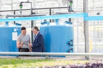Male botanist and businessman discussing by storage tank in greenhouse