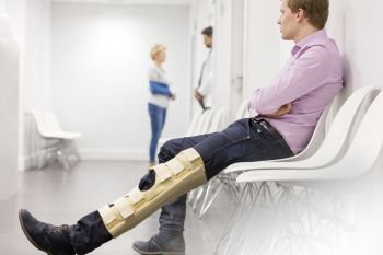 Man with brace on knee sitting in waiting room at hospital