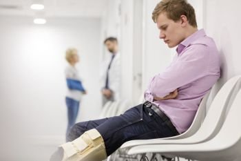 Man looking at brace on knee while sitting in hospital waiting room