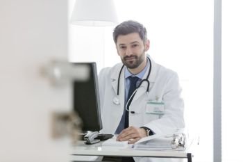Portrait of confident doctor using computer at desk in hospital