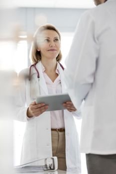 Smiling doctor holding digital tablet while discussing with colleague at hospital