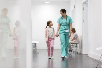 Smiling nurse walking with girl in corridor at hospital