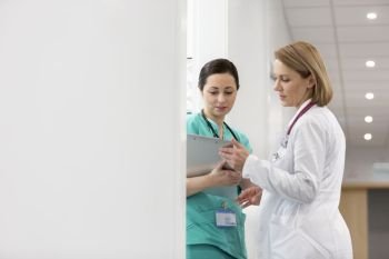 Mature doctor discussing with nurse over medical report on clipboard at hospital