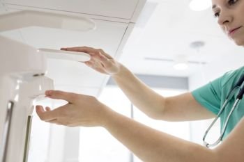 Doctor cleaning hands with anti-bacterial sanitizer dispenser in hospital