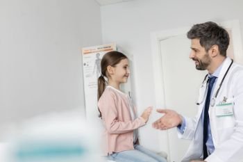 Smiling mid adult doctor shaking hands with girl patient at hospital