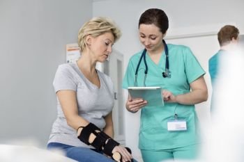 Nurse showing medical report on digital tablet to woman with braced hand