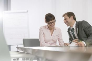 Smiling mid adult business colleagues discussing while sitting at conference table in boardroom