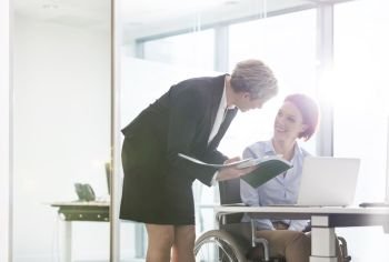 Mature businesswoman discussing over document with disabled colleague at desk in office