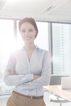 Portrait of smiling young businesswoman standing with arms crossed in boardroom at office