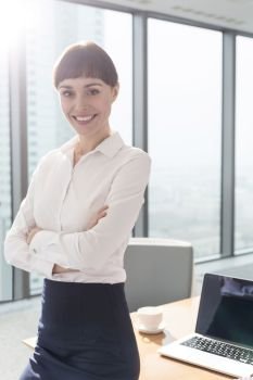 Portrait of smiling businesswoman sitting with arms crossed on table in boardroom at office