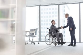 Businessman shaking hands with smiling disabled colleague in boardroom at office