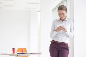 Smiling young businesswoman using smartphone while standing at new office