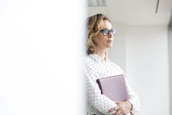 Thoughtful businesswoman holding file while looking away in new office