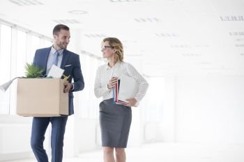 Smiling business carrying cardboard box while talking with colleague at new office