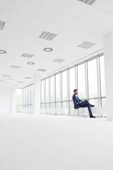 Full length side view of businessman sitting on chair at new empty office
