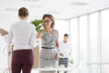 Businesswoman and colleague standing with box at desk in new office