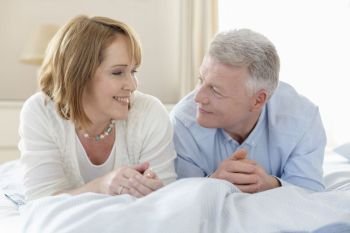 Smiling mature couple looking at each other while lying on bed