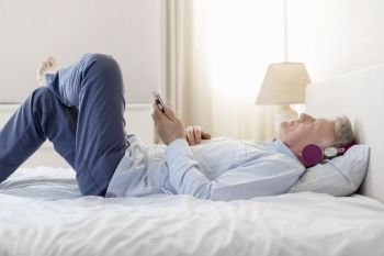 Side view of man listening music while lying on bed at home