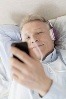 Mature man looking at smartphone while lying on bed at home