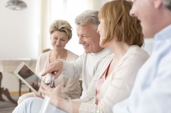 Smiling mature man holding digital tablet while sitting with friends at home