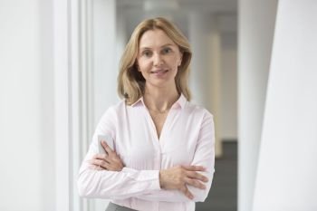 Portrait of confident businesswoman standing with arms crossed in corridor at office