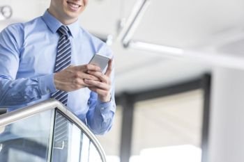 Midsection of smiling businessman using smartphone while standing at office