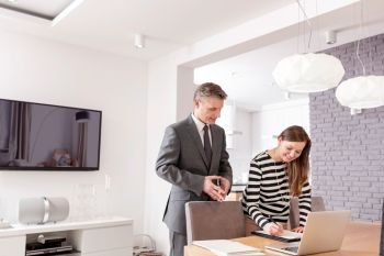 Smiling woman signing contract while standing by mature male realtor at table in apartment