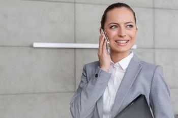 Smiling young female realtor looking away while talking on mobile phone in apartment