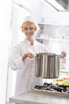 Portrait of smiling chef holding steel pot over stove in kitchen at restaurant
