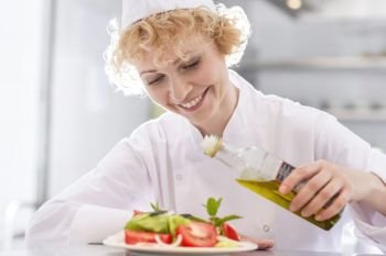 Smiling mature chef pouring oil on salad in plate at restaurant