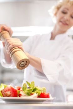 Mature chef using peppermill on salad in plate at restaurant