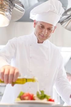 Confident mature chef using pouring oil on salad in plate at restaurant
