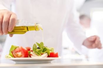 Midsection of mature chef using pouring oil on salad in plate at restaurant