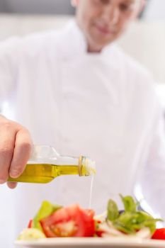 Mature chef using pouring oil on salad in plate at restaurant
