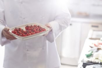 Midsection of chef holding fresh cherry tomatoes in tray at restaurant