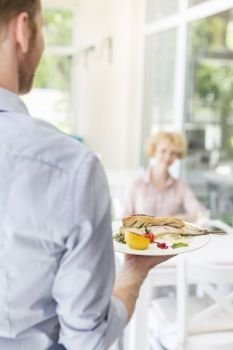 Waiter serving lunch to mature customer sitting at table in restaurant