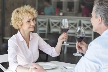 Smiling mature couple toasting wineglasses while sitting at table in restaurant