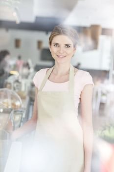 Portrait of smiling beautiful young waitress standing by counter at restaurant