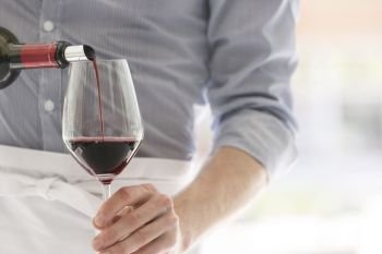 Midsection of waiter pouring red wine in wineglass at restaurant