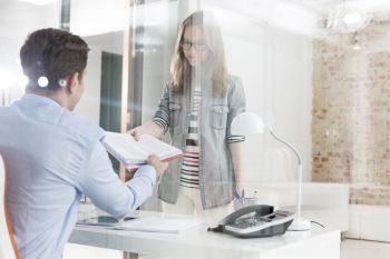 Midsection of young businesswoman giving documents to manager in office