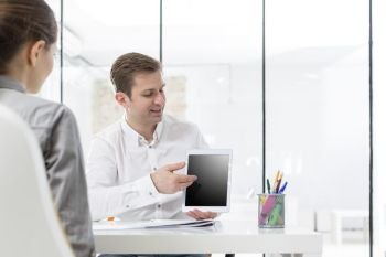 Mid adult businessman showing digital tablet to colleague in office