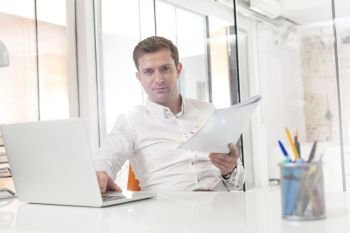 Portrait of creative businessman with laptop and documents in office