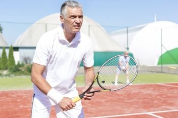 Confident mature man standing with tennis racket against friend playing doubles match on court