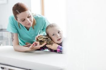 Doctor looking at girl listening to turtle at veterinary clinic