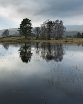 Beautiful landscape image of moody storm clouds over Kelly Hall Tarn in Lake District during late Autumn Fall afternoon
