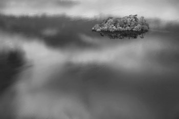 Black and white Abstract landscape Autumn image of view of islands in Derwentwater with sky reflections isolating them with vibrant Fall colors
