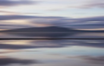 Intentional camera movement sunset landscape image of distant mountains with pastel colors reflected in the calm ocean