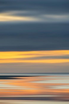 Intentional camera movement sunset landscape image of distant mountains with pastel colors reflected in the calm ocean